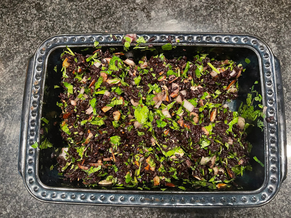 Black rice with sliced almonds and fresh cilantro in a dark baking dish