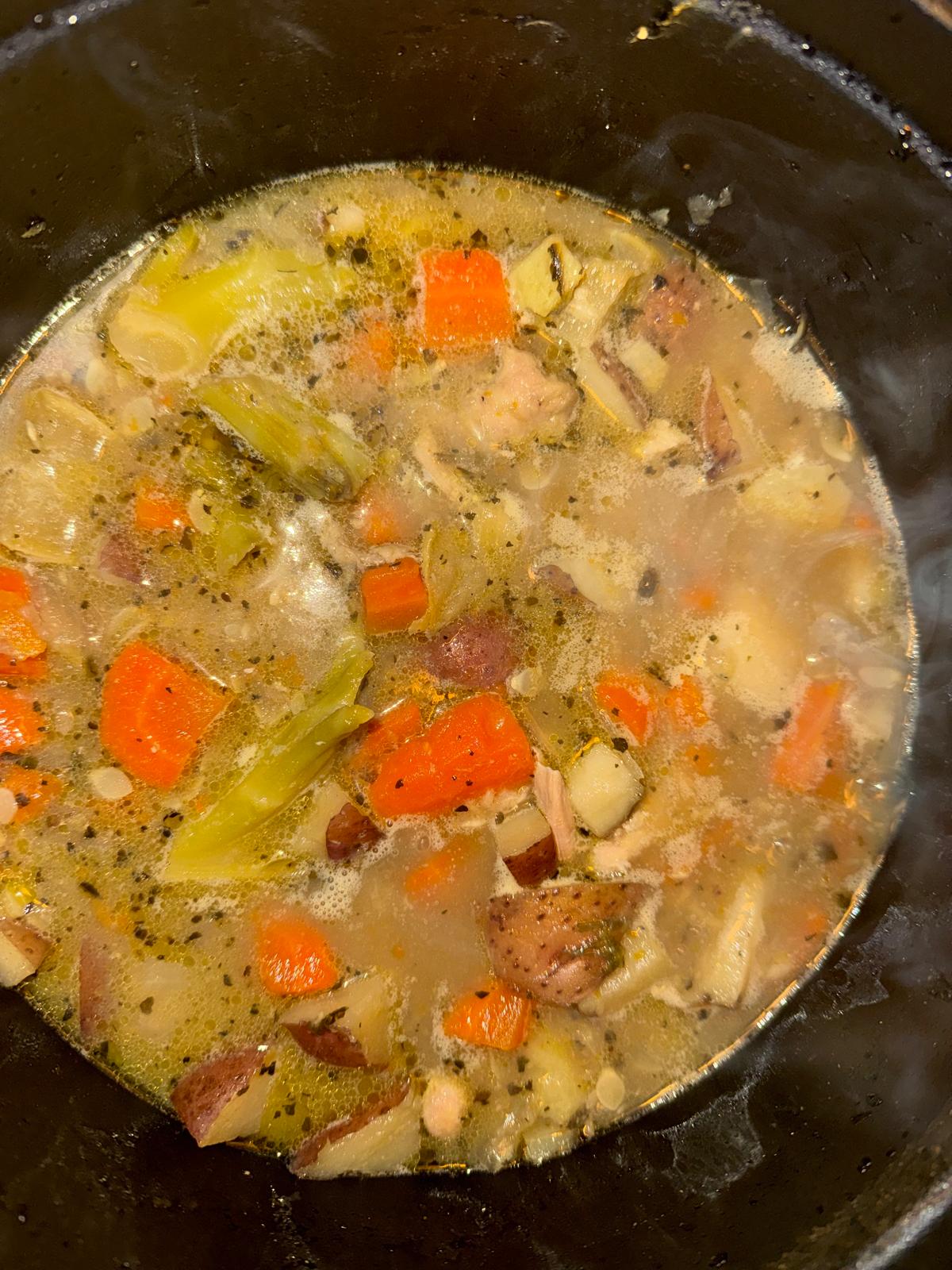 Nourishing chicken soup with carrots, celery, and potatoes simmering in a pot.