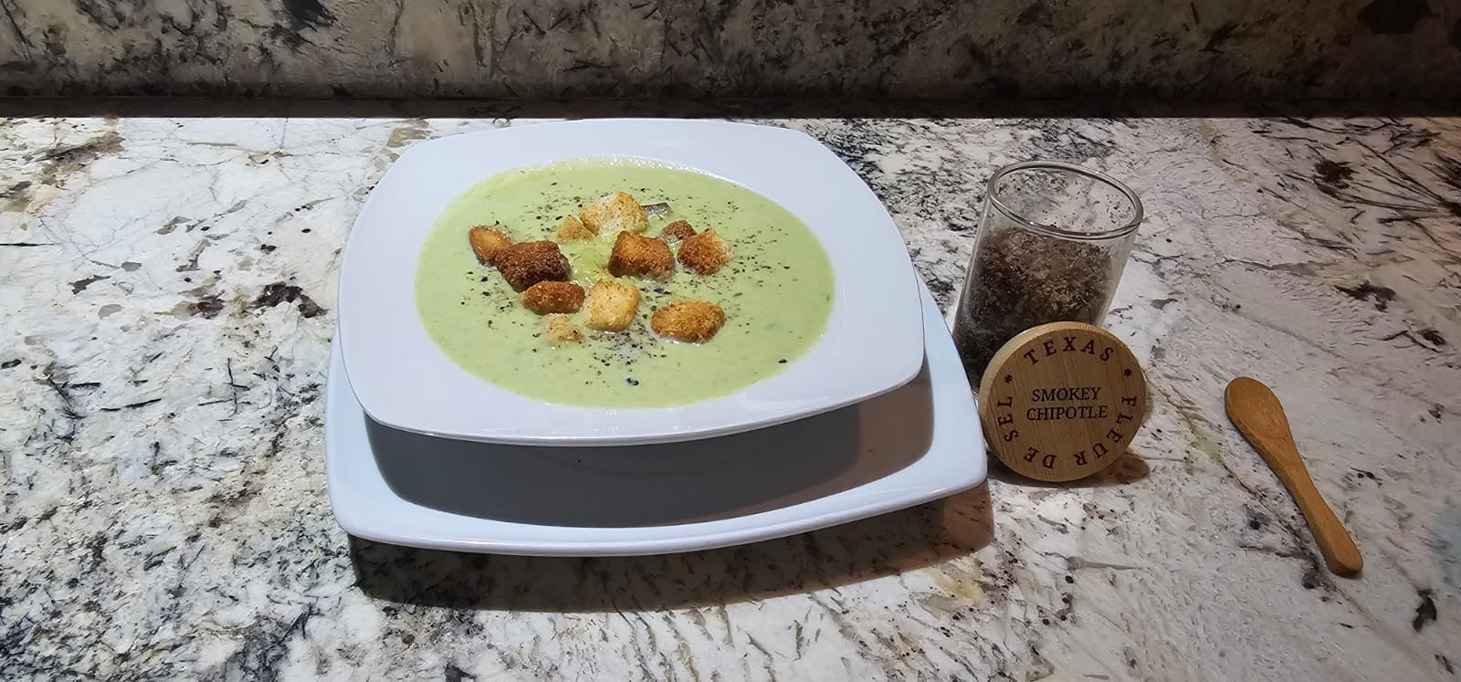 Creamy asparagus soup with croutons, smokey chipotle seasoning on marble countertop