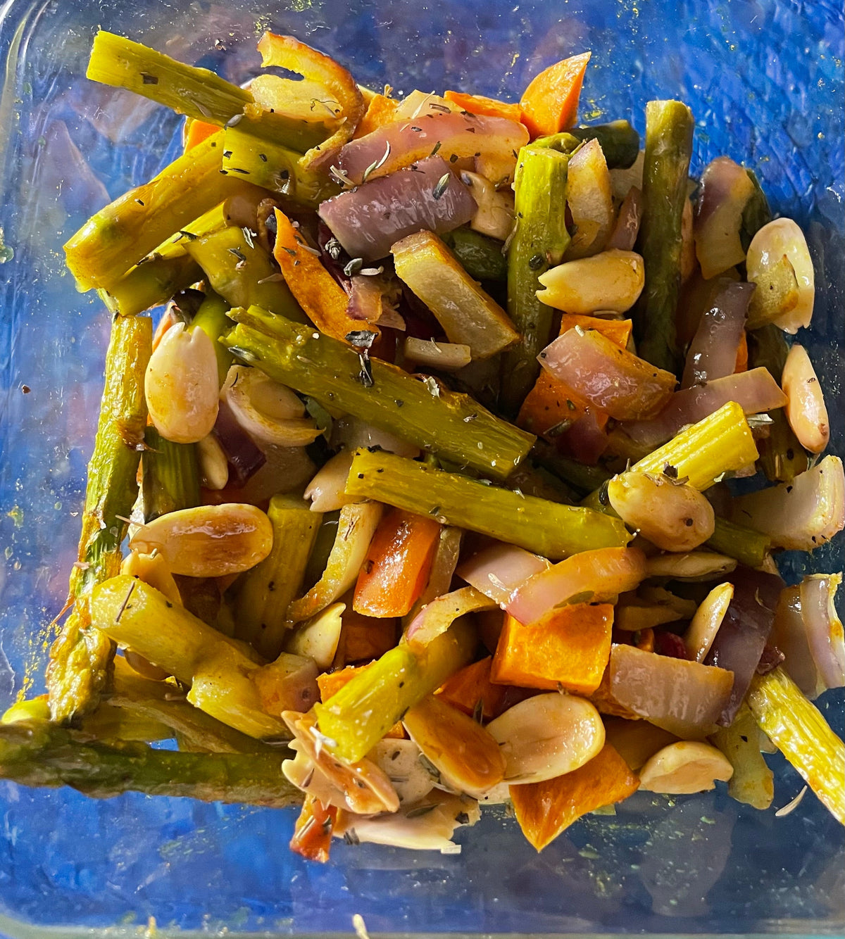 Roasted asparagus, carrots, and red onion seasoned with Fleur de Sel salt in a blue container.