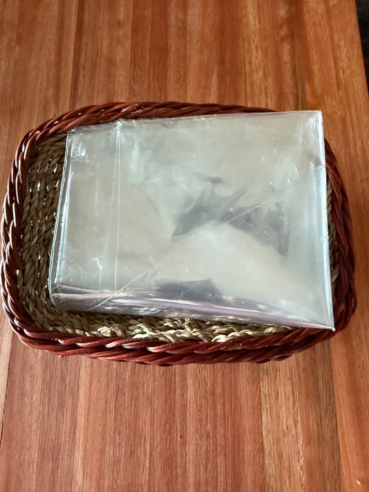 A cellophane wrapped gift basket containing items, placed inside a red and brown wicker basket, with a wooden surface in the background.