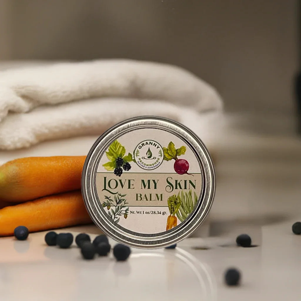 Herbal skincare balm tin labeled 'Love My Skin Balm' with carrots, berries, and towel in background