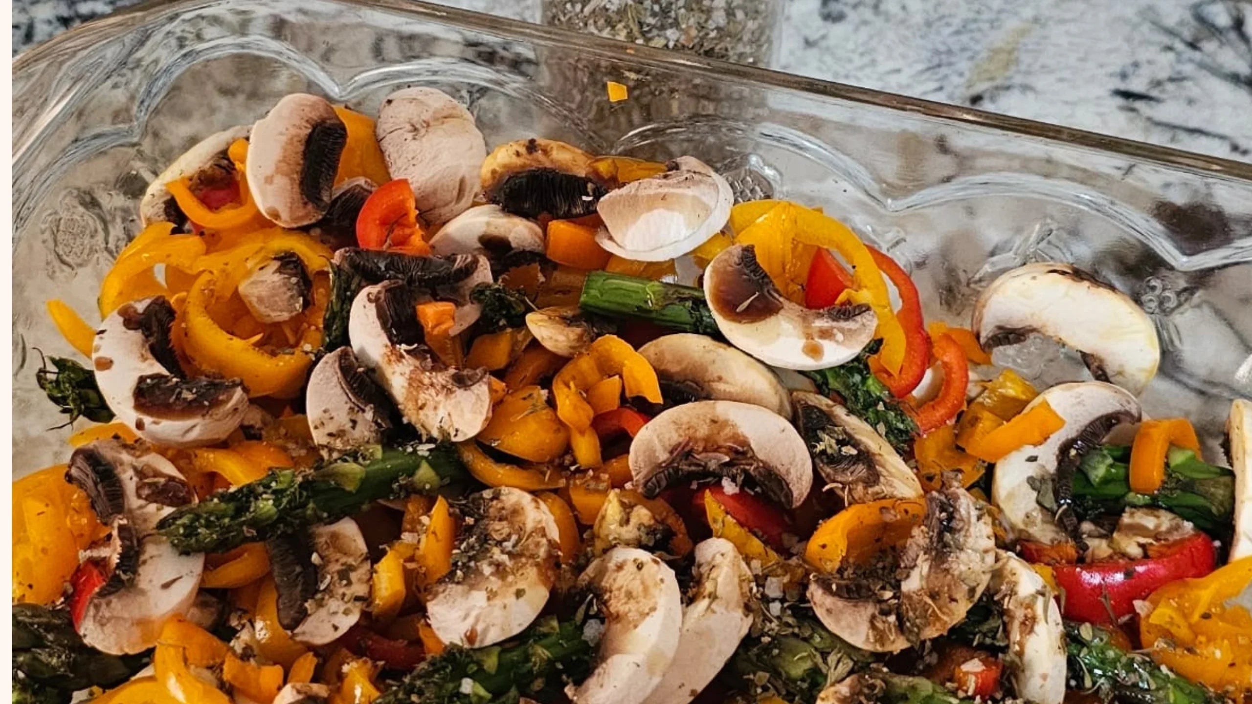 Sliced mushrooms, bell peppers, and asparagus in a glass baking dish on a kitchen countertop