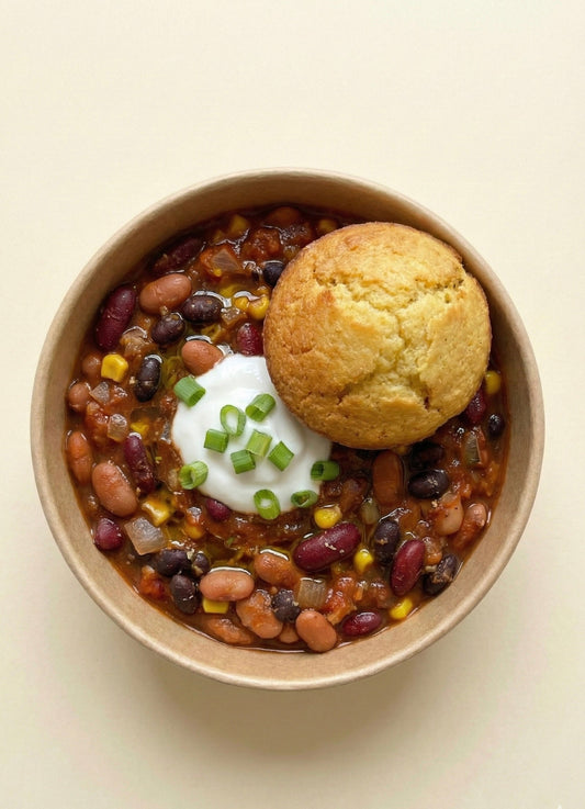 Bowl of three bean chili with corn, sour cream, scallions, and cornbread on top