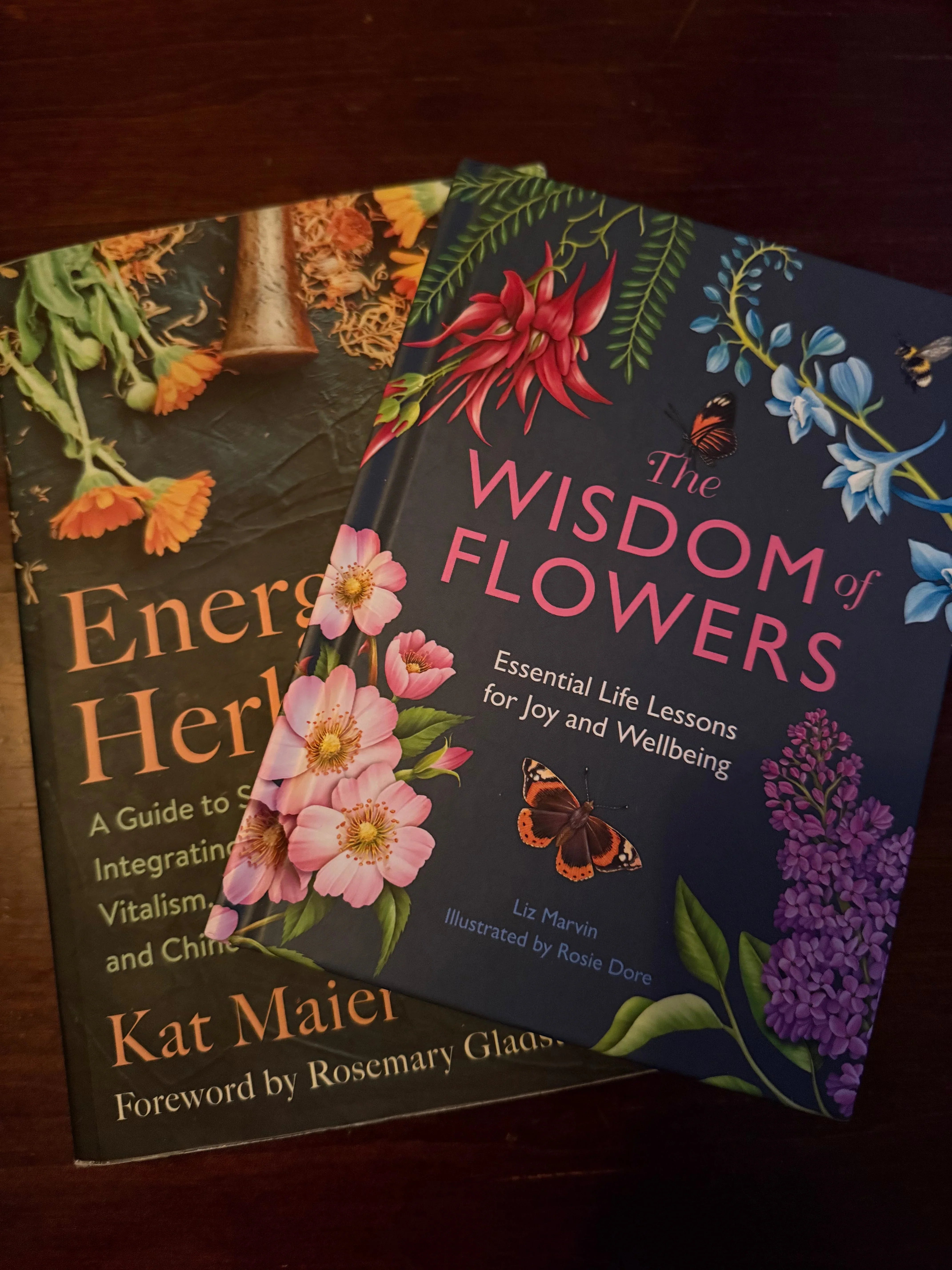 Two botanical books with colorful flower illustrations on a dark wooden table