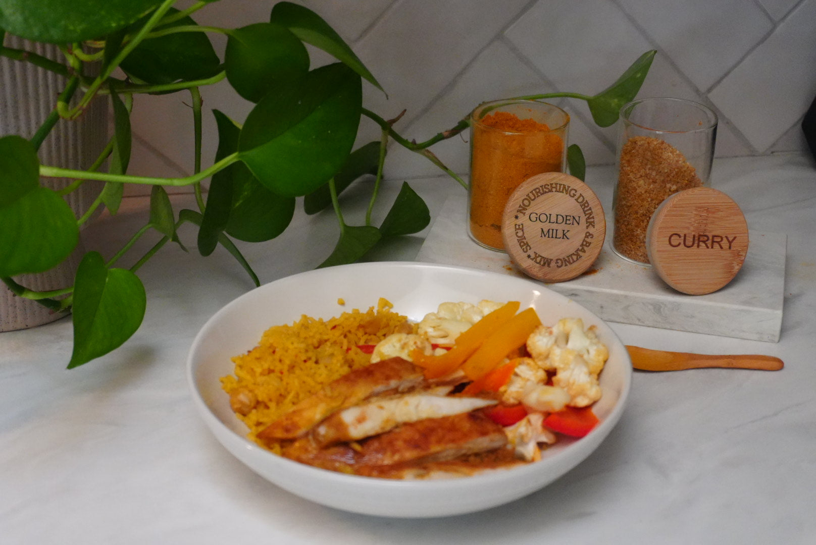 Bowl of golden rice, sliced chicken, and vegetables with curry and golden milk spices on countertop