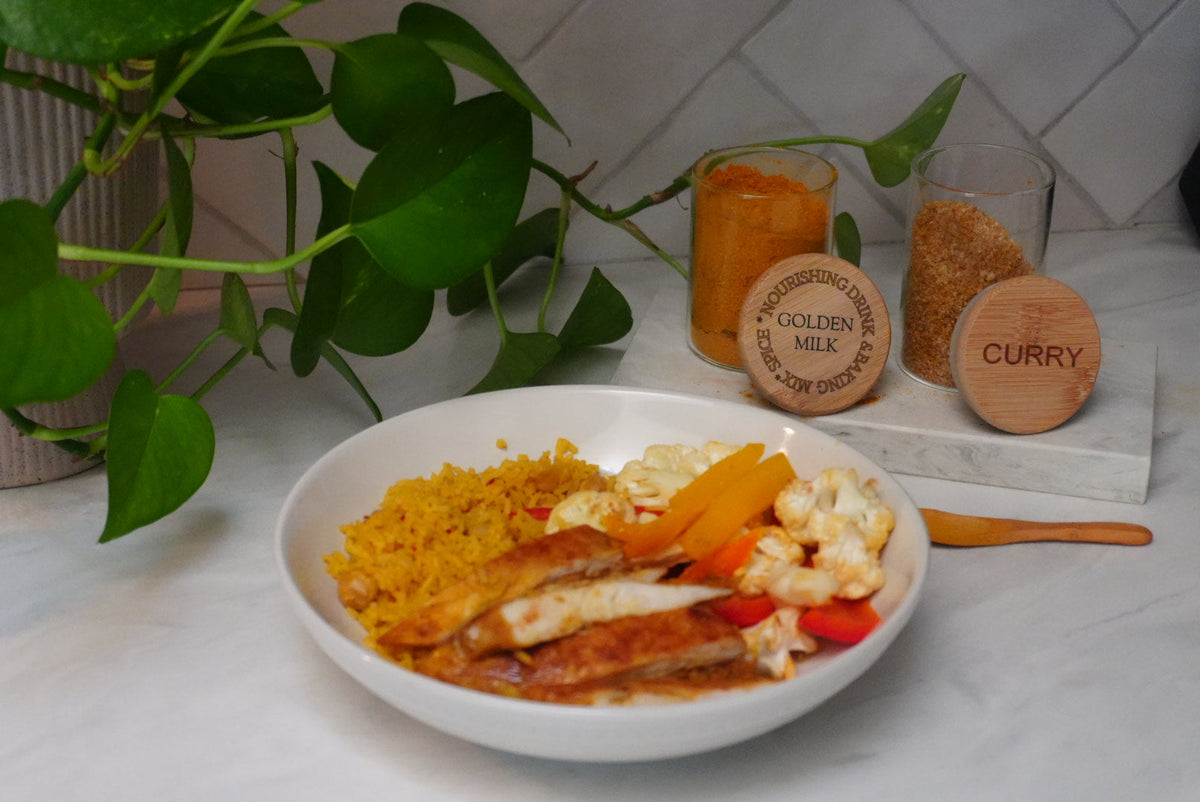 Curry chicken bowl with yellow rice and vegetables next to Golden Milk and Curry spice mixes