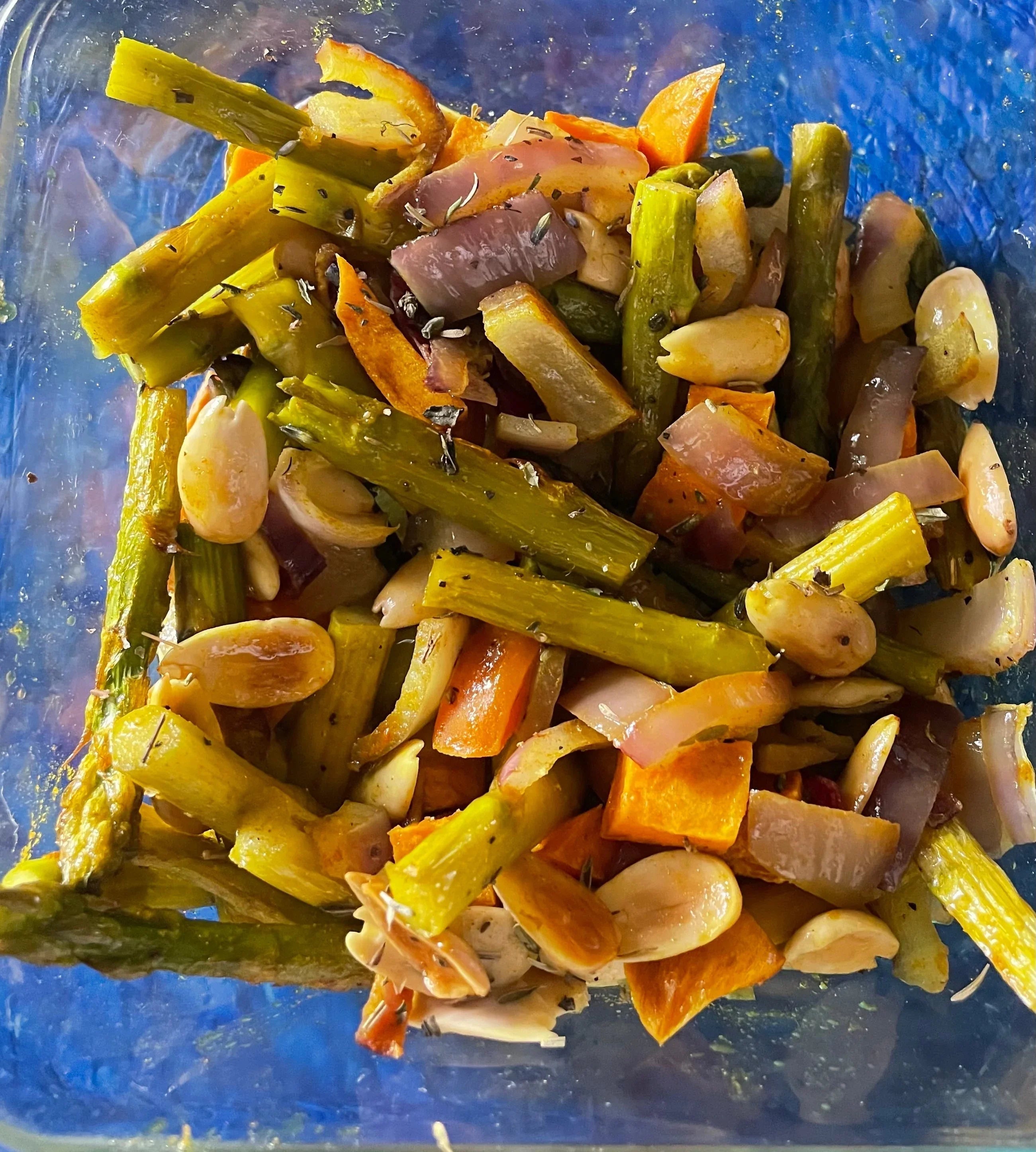 Roasted asparagus, red onion, carrot, and garlic in a glass dish, seasoned with herbs