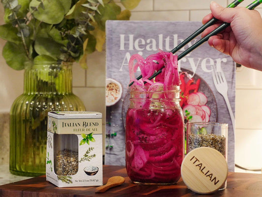 Pickled red onions in a glass jar with chopsticks, Italian blend seasoning, cookbook in kitchen