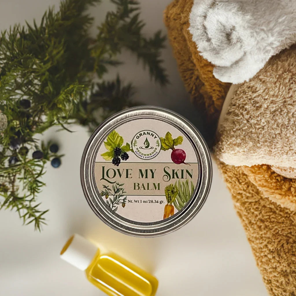 Herbal Love My Skin balm tin with body care items, greenery, and essential oil bottle